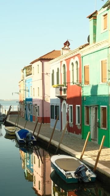 Brightly colored houses in blue, pink, red, and green lining a quiet canal with moored boats