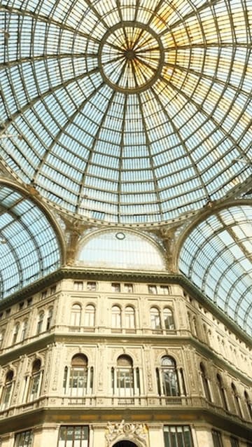 A vast glass and iron dome ceiling arching over an ornate stone gallery building
