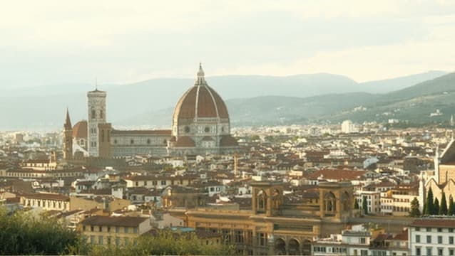 A hilltop view over a terracotta-roofed city with a great cathedral dome at its center