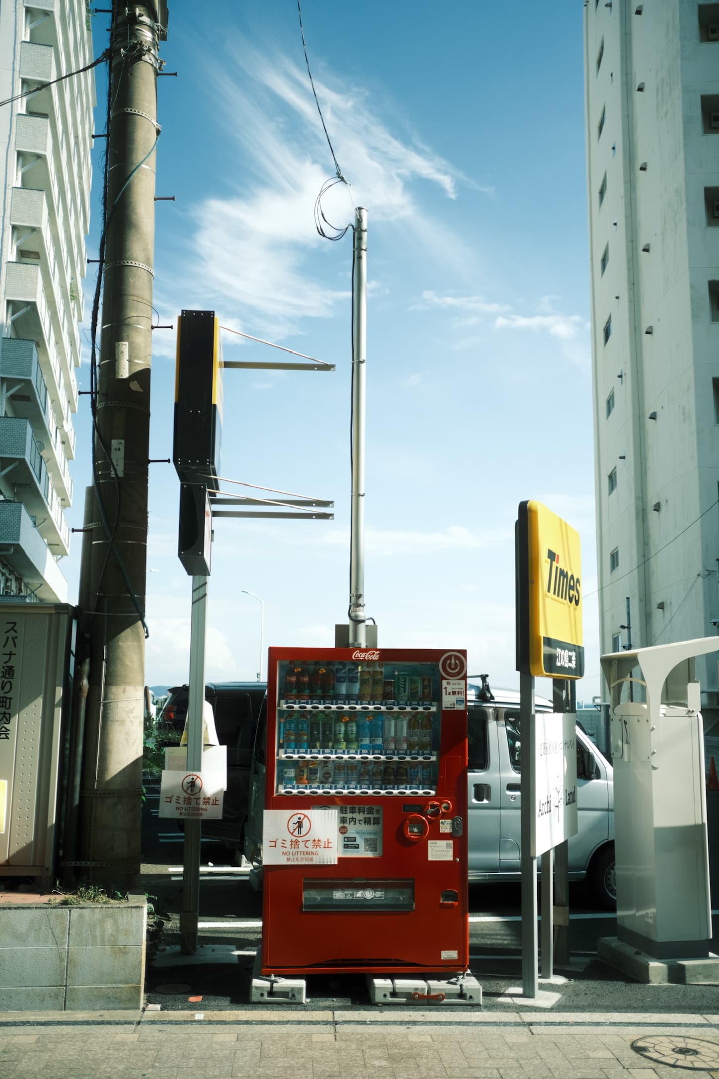 A red Coca-Cola vending machine on a quiet street corner under a bright blue sky