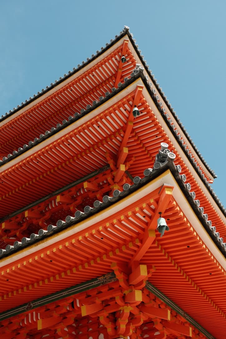 The vermilion eaves of a wooden pagoda seen from below against a clear sky